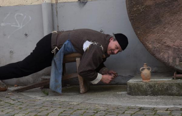Der Edelsteinschleifer (Bernd Wintermantel) geht auf seinem Kürass liegend unter dem großen Schleifstein seiner Arbeit nach. Der Edelsteinschleifer (Bernd Wintermantel) geht auf seinem Kürass liegend unter dem großen Schleifstein seiner Arbeit nach.
